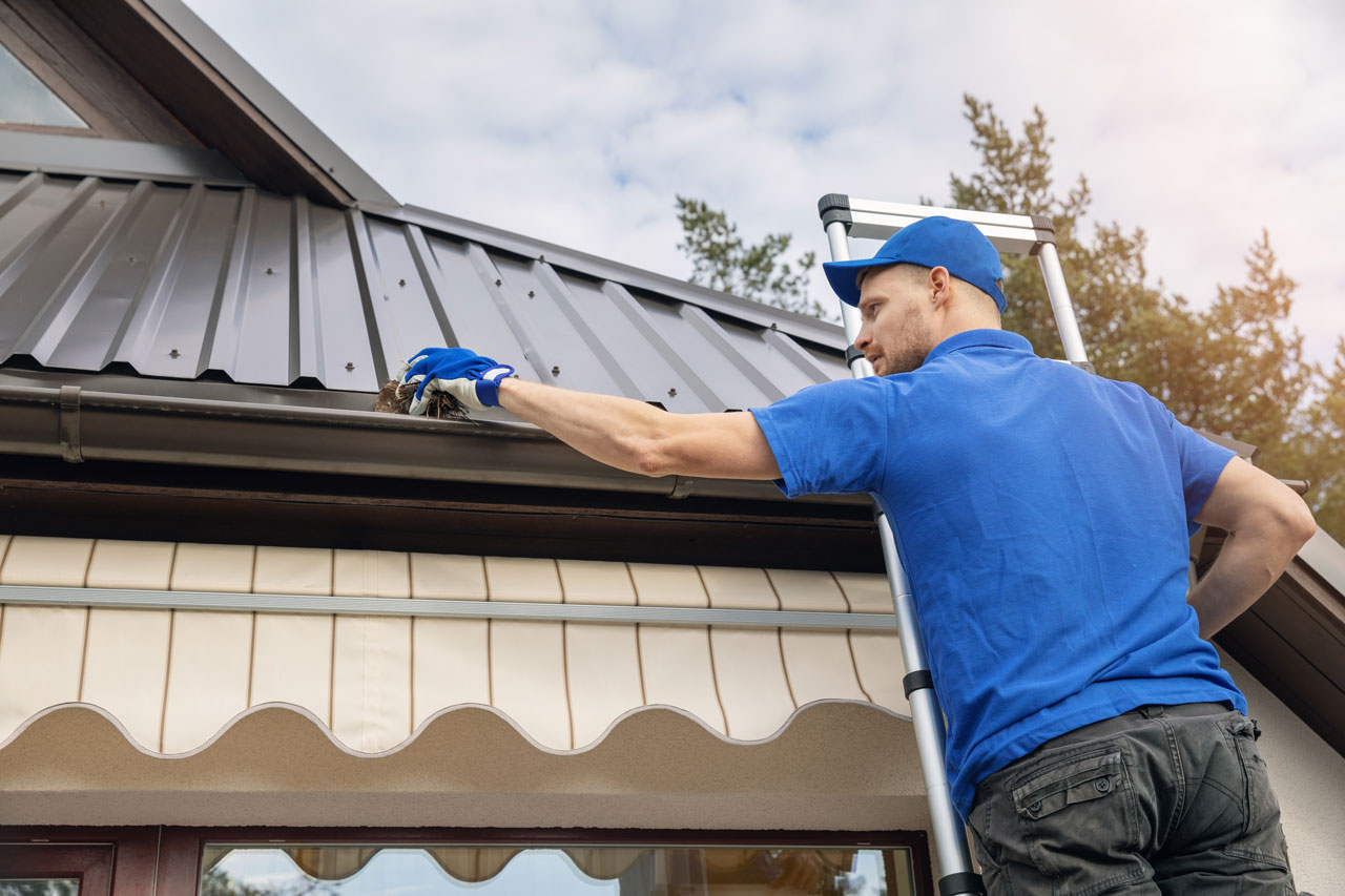 A professional installing gutter using a power drill on a house exterior