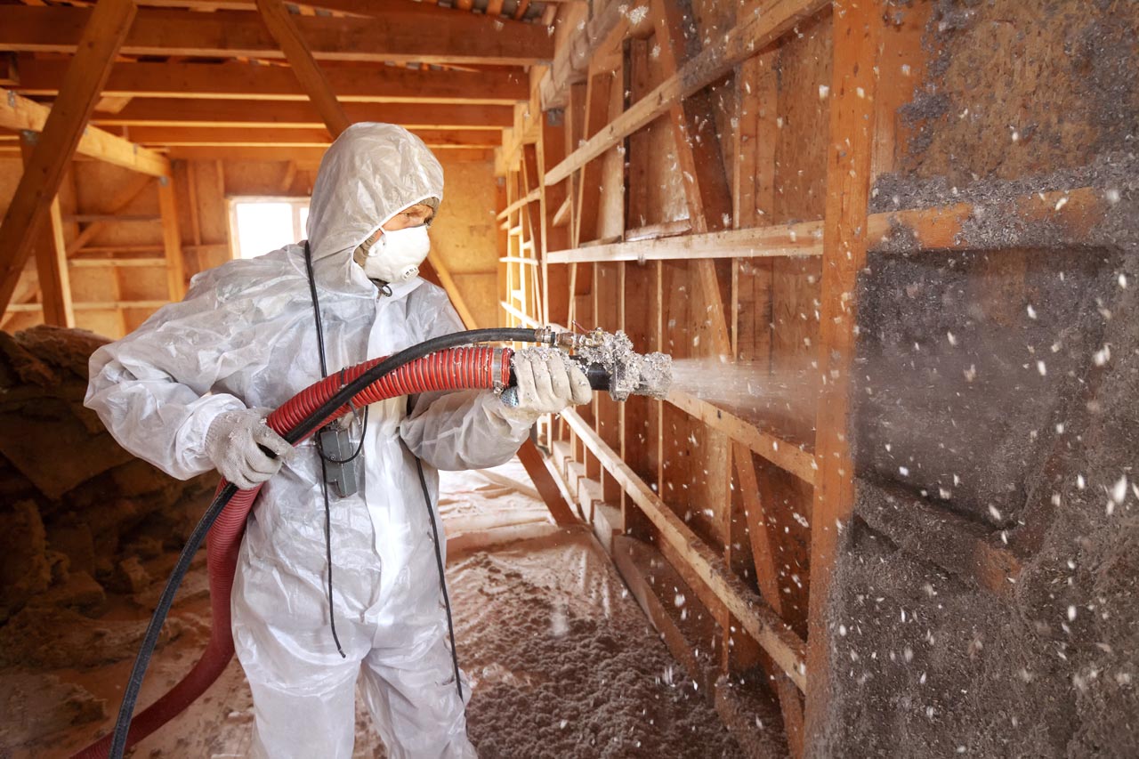 A worker on full protective gear doing spray foam insulation on an attic of a house
