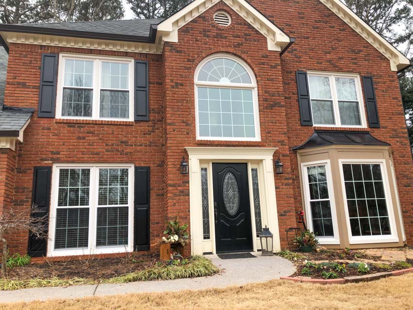 Two-story red brick home with new white replacement windows, black shutters, and arched transom window above the entrance